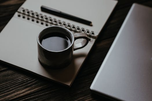 A laptop on a desk with a notepad and coffee, ready for writing